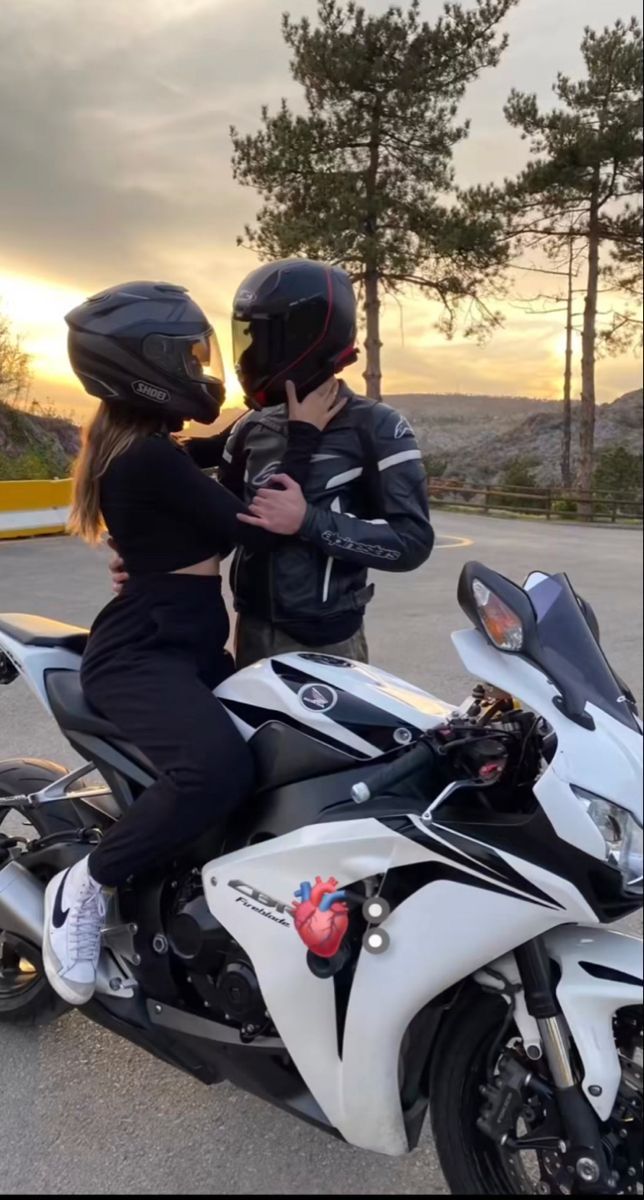 a man and woman sitting on a motorcycle in the parking lot at sunset or dawn