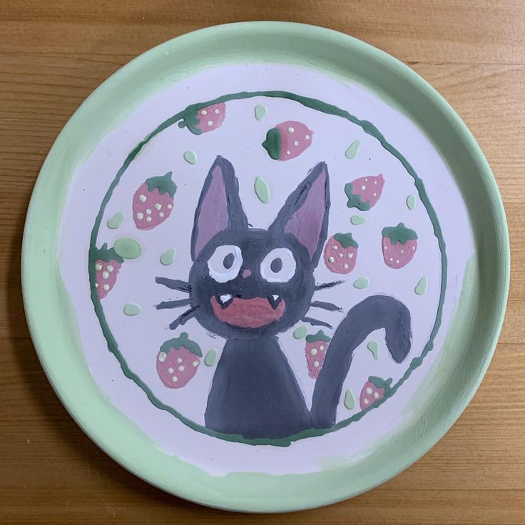 a black cat painted on a plate with strawberries