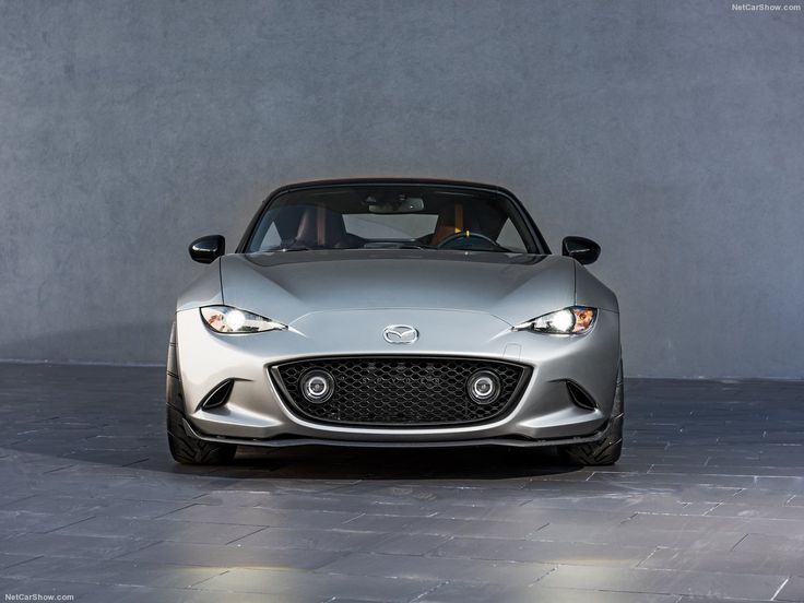 the front end of a silver sports car parked in an empty room with concrete walls