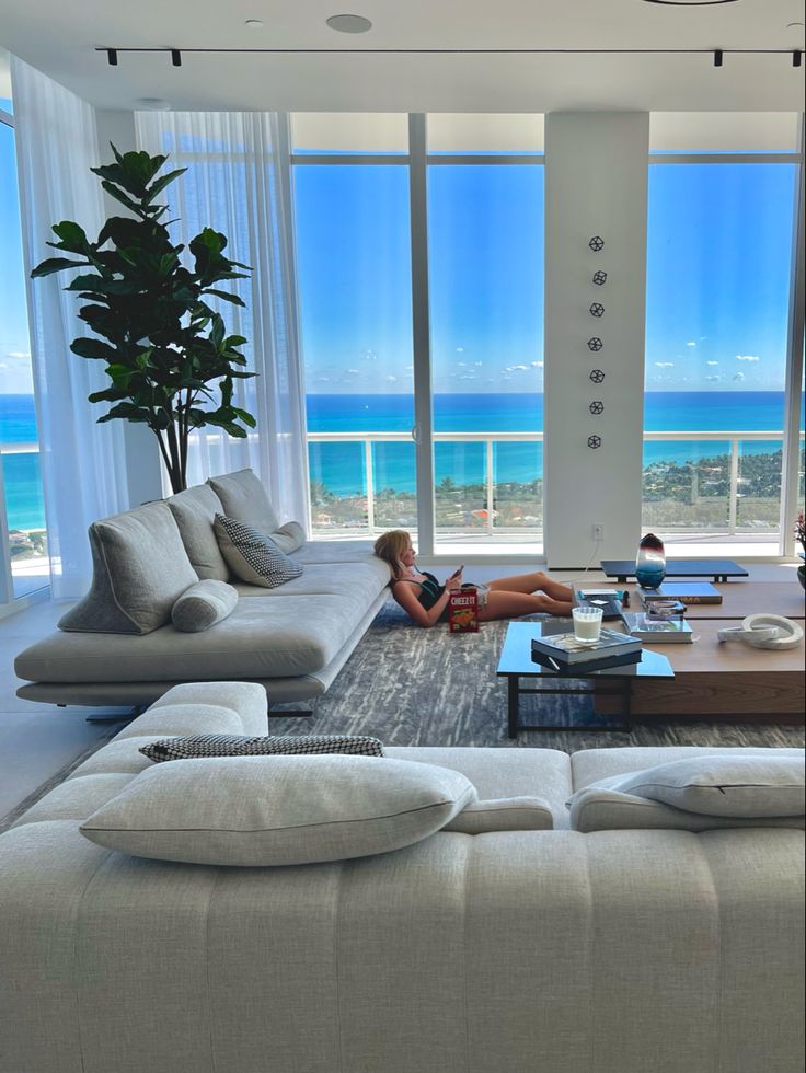 a woman laying on top of a couch in a living room next to large windows