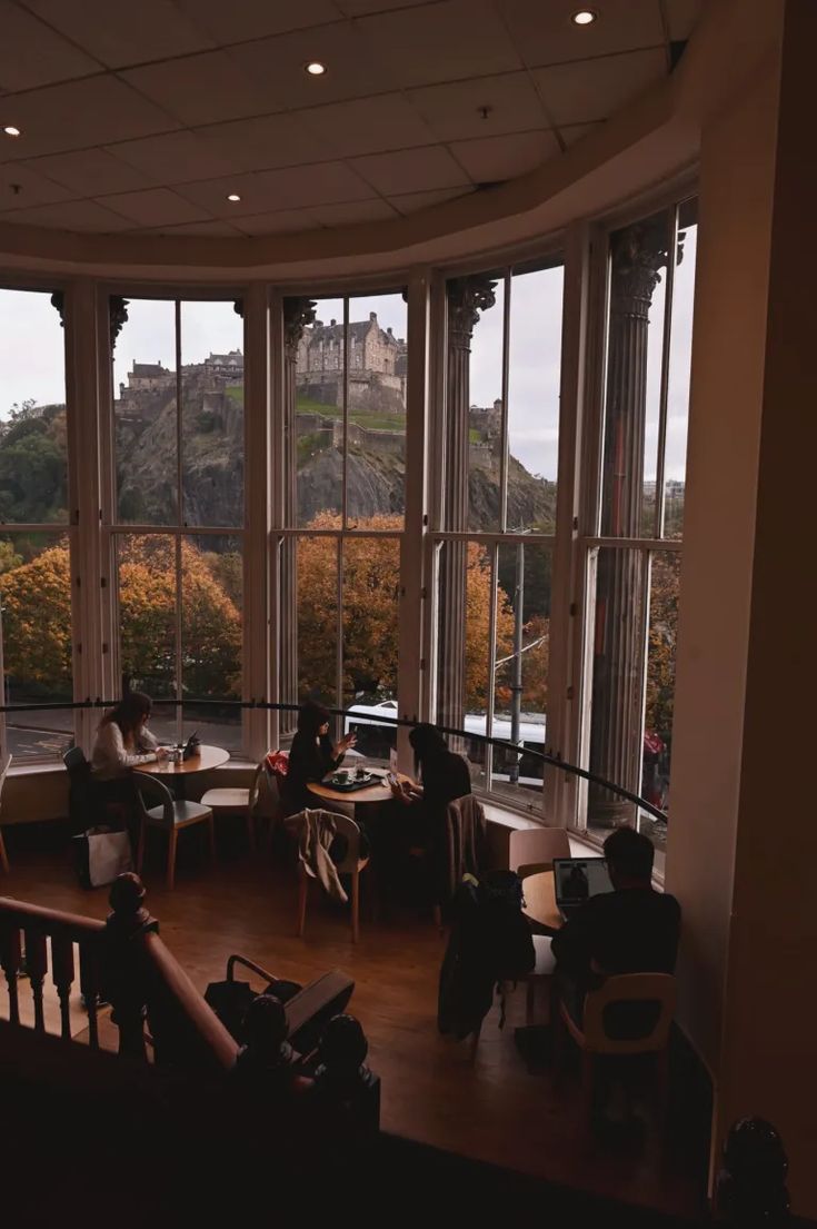 two people sitting at tables in front of large windows looking out onto the hills outside