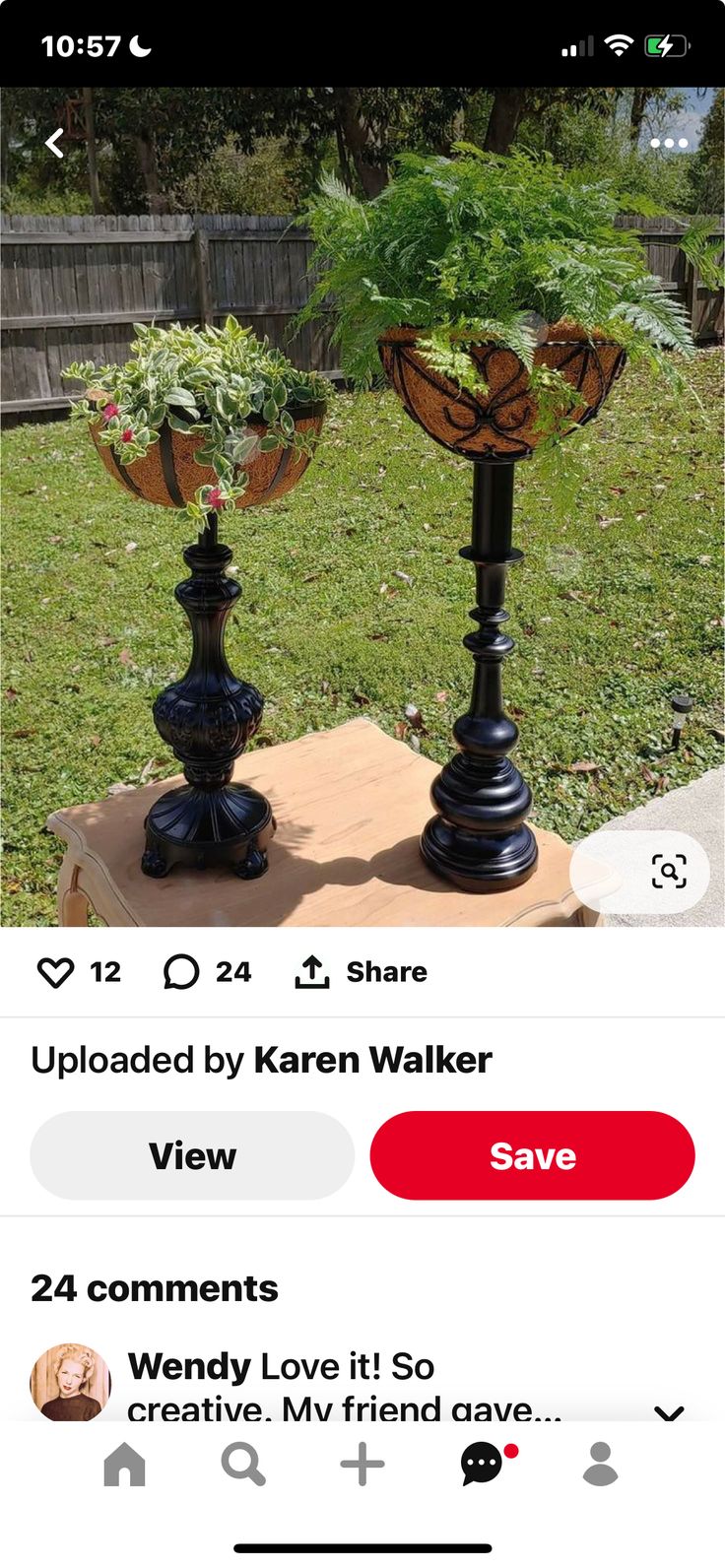 two black vases with plants in them sitting on top of a wooden table next to grass