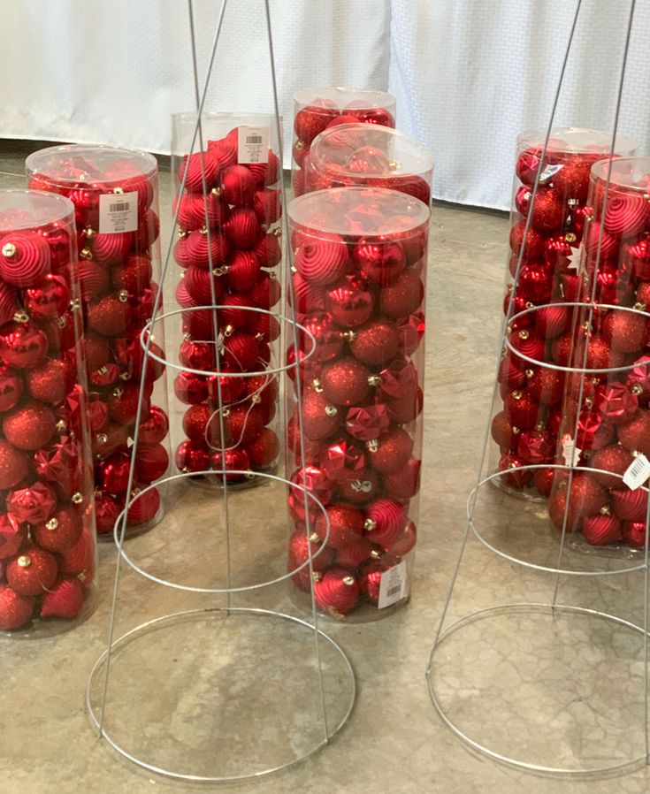 red ornaments are in clear containers on the table with tags attached to them and hanging from metal poles