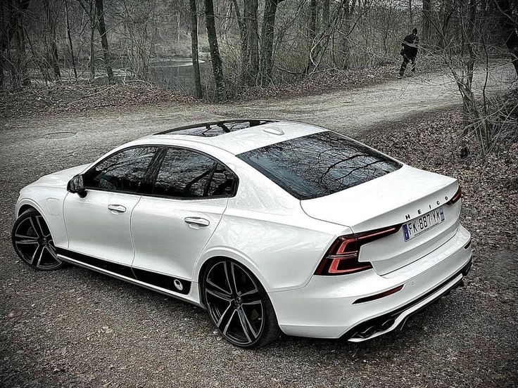 a white car parked on the side of a dirt road in front of some trees