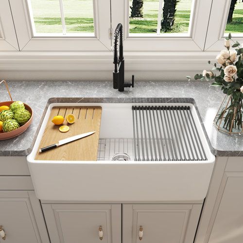 a kitchen sink with cutting board, knife and bowl of fruit on the counter top