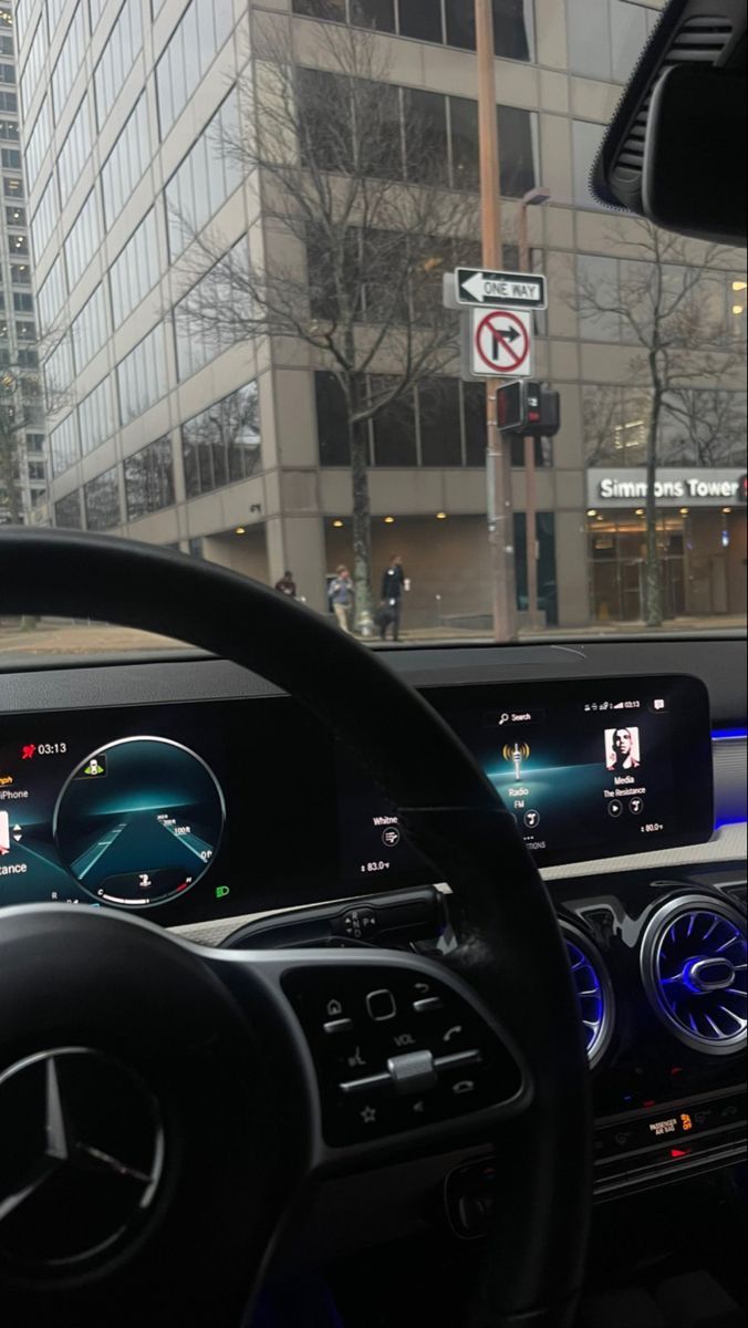 the interior of a car with electronic dashboards and steering wheel controls in front of tall buildings