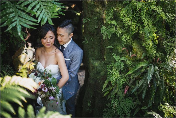 a bride and groom standing next to each other in front of green plants at their wedding