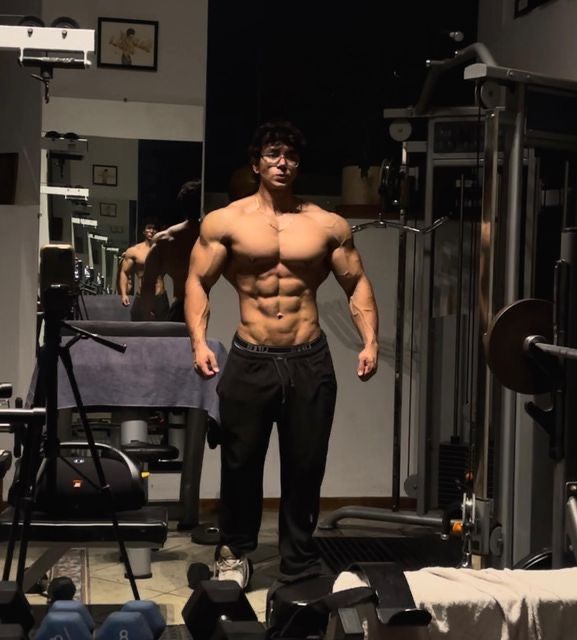 a shirtless man standing in front of a gym machine with his hands on his hips