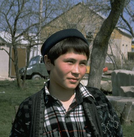 a young man standing in front of a tree wearing a plaid shirt and black hat