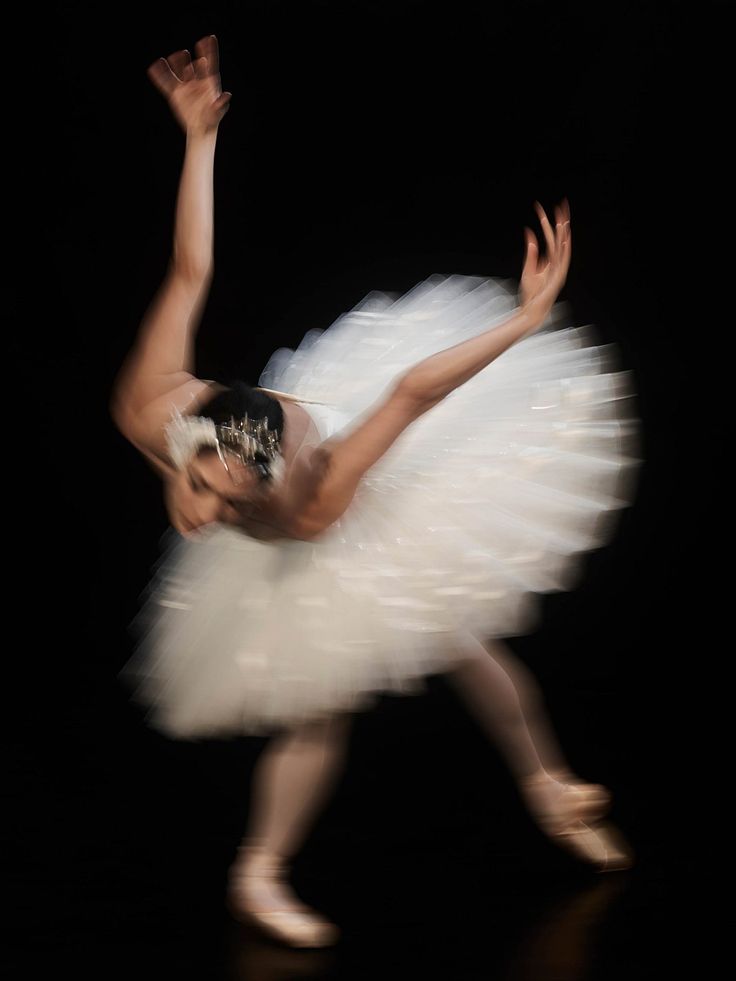 a ballerina in white tutu with her arms up and legs spread out, while she is dancing