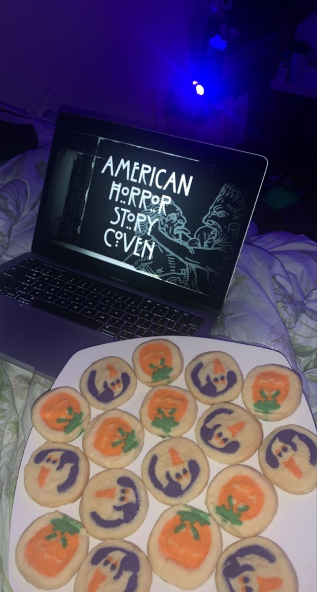 an open laptop computer sitting on top of a white plate filled with halloween themed cookies