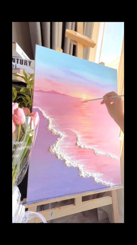 someone is painting on an easel with flowers in the foreground and water in the background