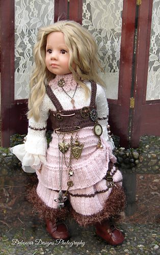 a doll wearing a pink dress and brown boots standing in front of a wooden door