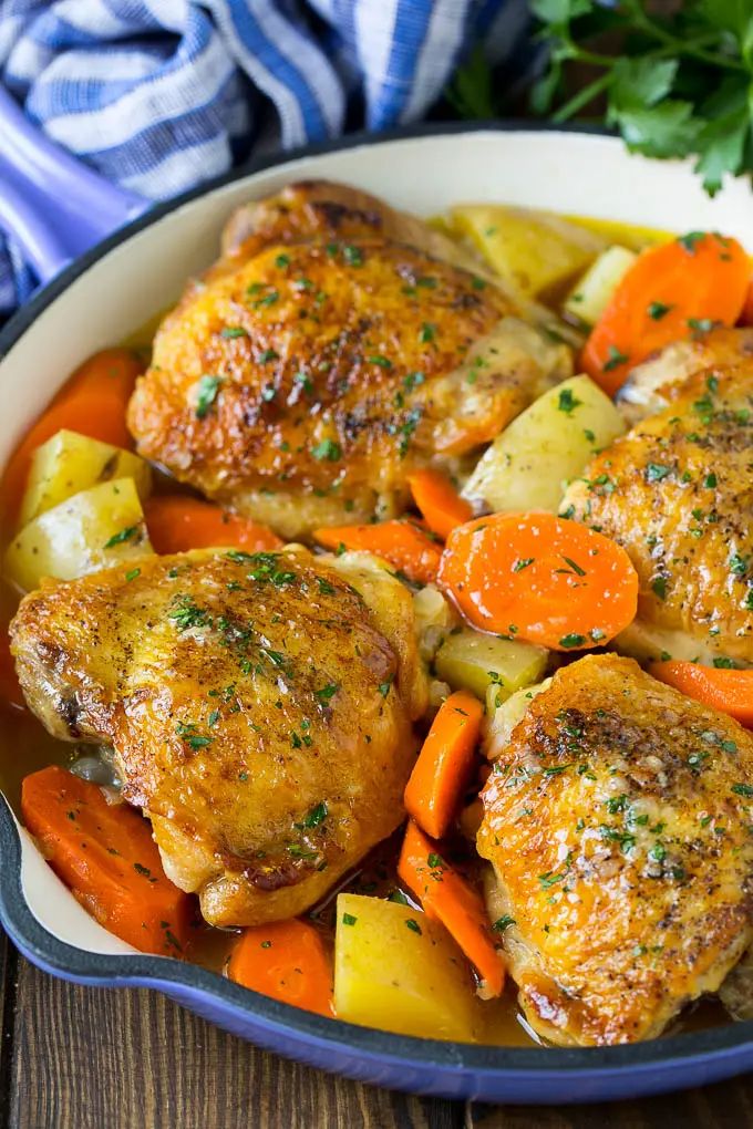 chicken, carrots and potatoes in a pan on a wooden table with parsley