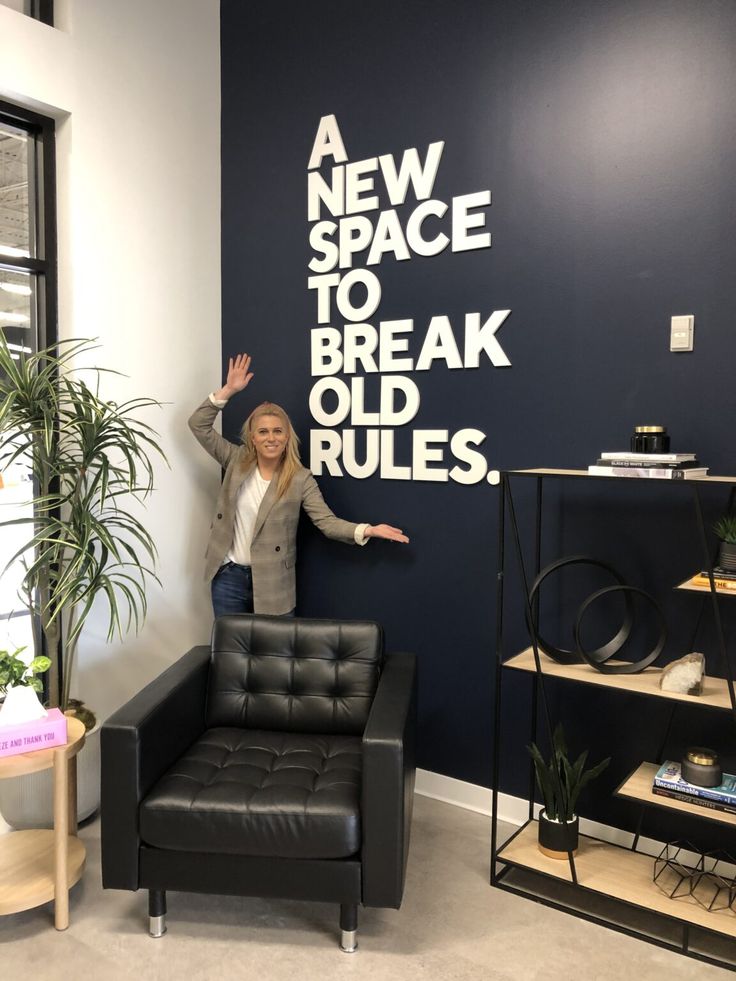 a woman standing next to a black chair in front of a wall that says a new space to break old rules