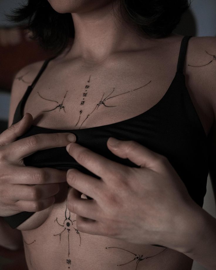 a woman with tattoos on her chest is looking at her cell phone while holding onto her bra