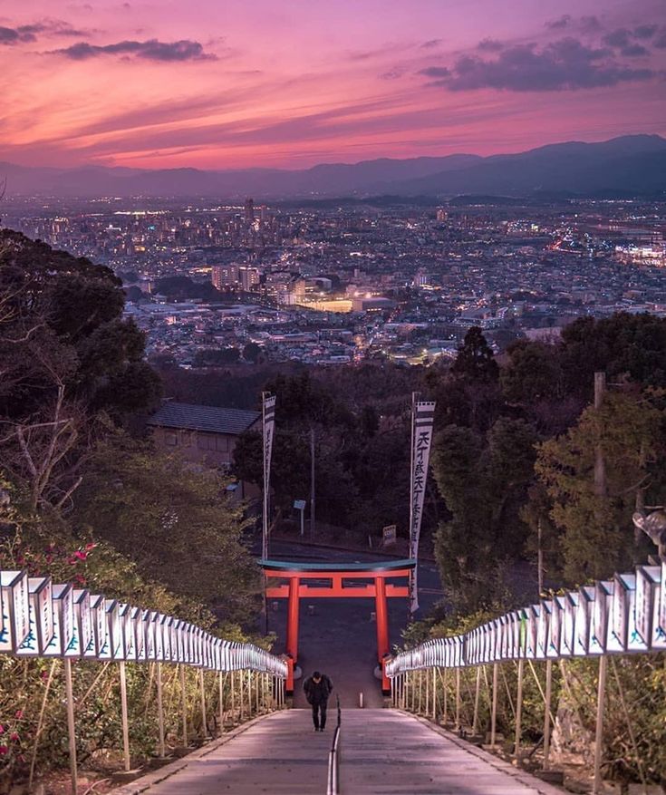 two people walking down a long narrow path in the middle of a city at sunset