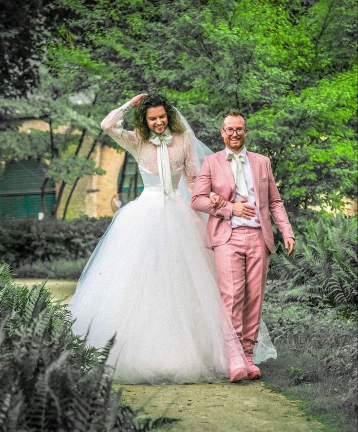 a bride and groom walking through the woods