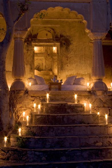 candles are lit on the steps leading up to a bed in an old building with stone walls