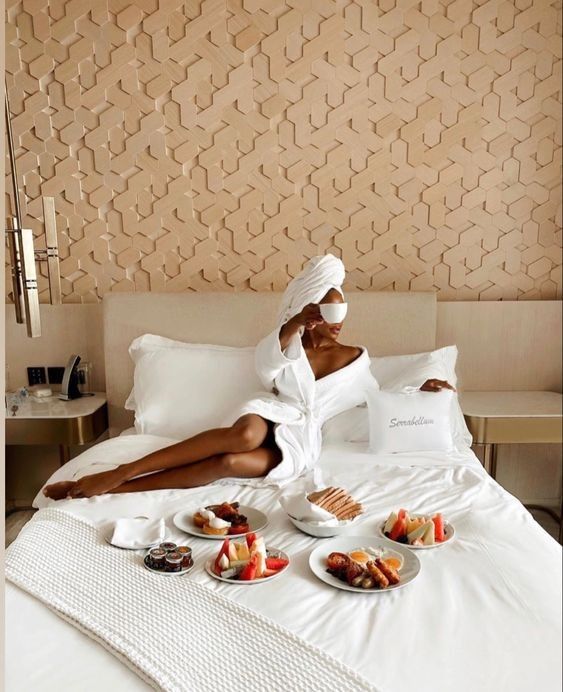 a woman sitting on top of a bed with plates of food in front of her