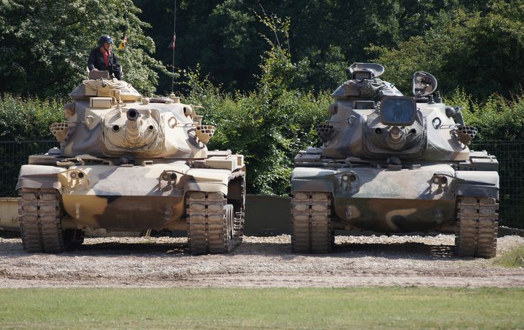 two army tanks sitting side by side in the dirt