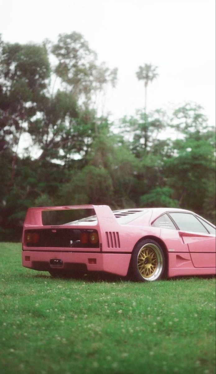 a pink sports car parked on top of a lush green field