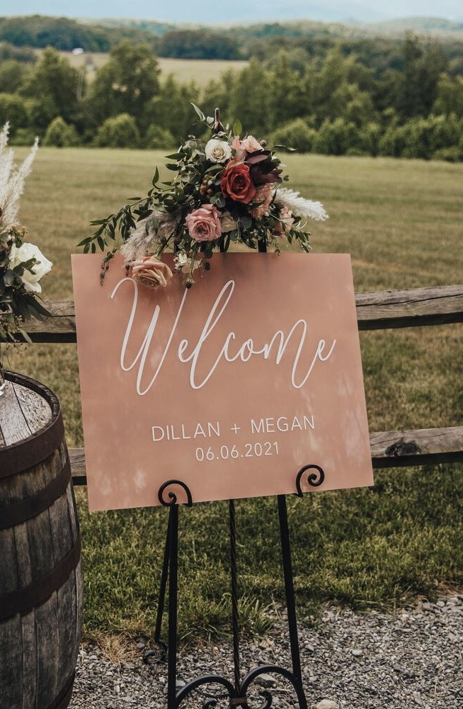 a welcome sign sitting on top of a metal stand next to a wooden barrel filled with flowers