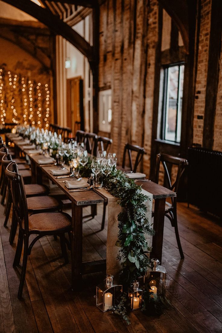 a long table set up with candles and greenery for a wedding reception at the barn