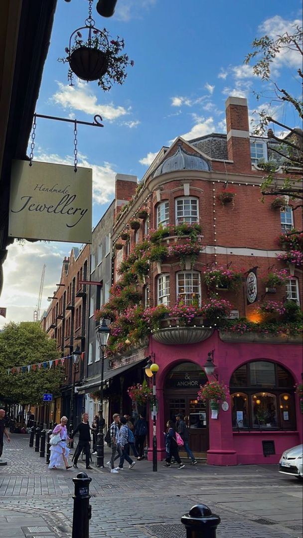 people are walking down the street in front of buildings with flowers growing on them and hanging from the roof