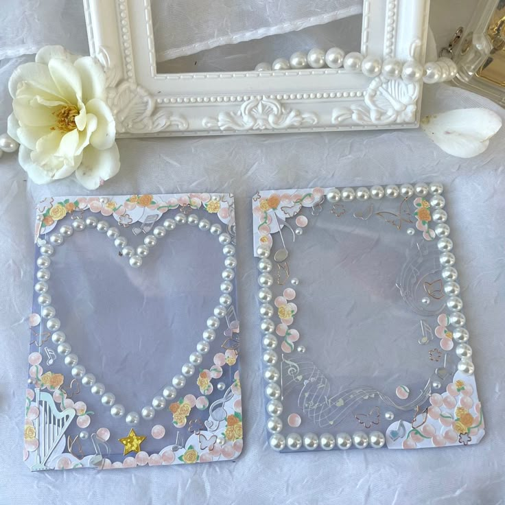 two decorative frames with pearls and flowers on a white tablecloth next to a flower