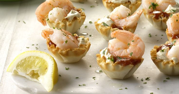 small appetizers with shrimp and cheese are on a white plate next to lemon wedges