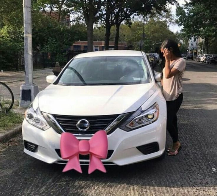 a woman standing next to a white car with a pink bow