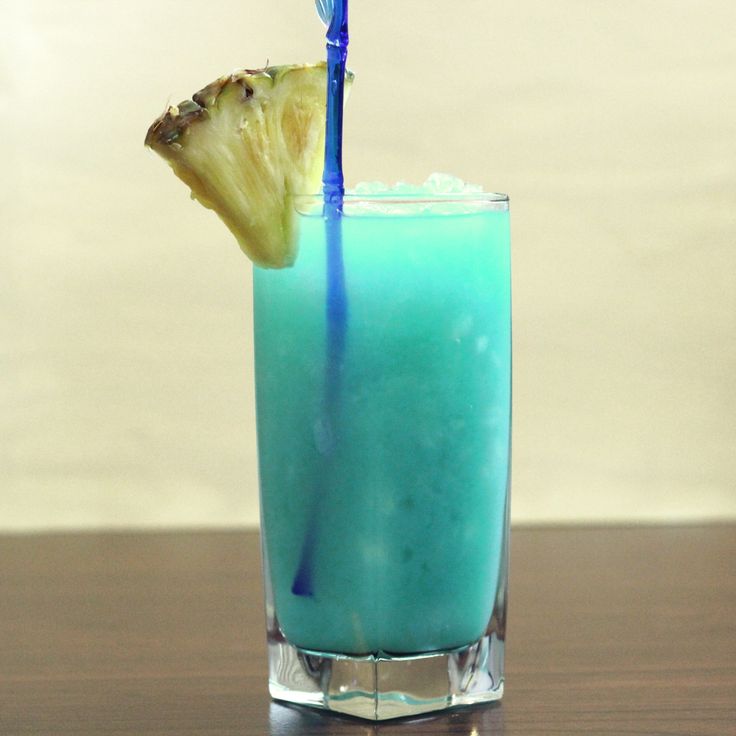 a blue drink with a slice of pineapple on the rim and a straw sticking out of it