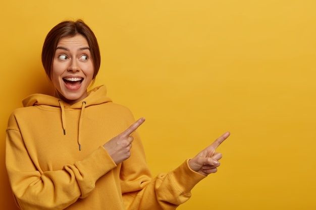 a woman in a yellow hoodie pointing to the side with her finger and smiling