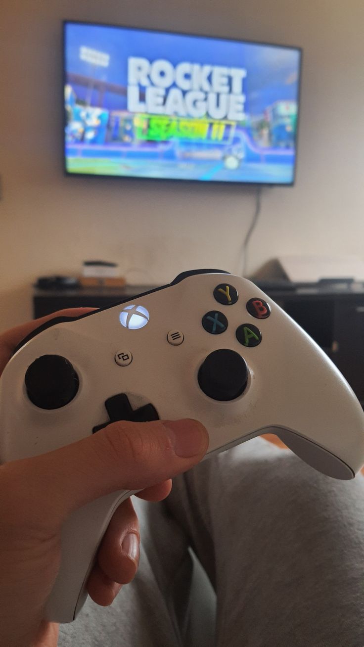 a person holding a video game controller in front of a tv with the rocket league logo on it