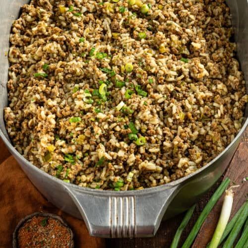 a pan filled with rice and vegetables on top of a wooden table next to green beans