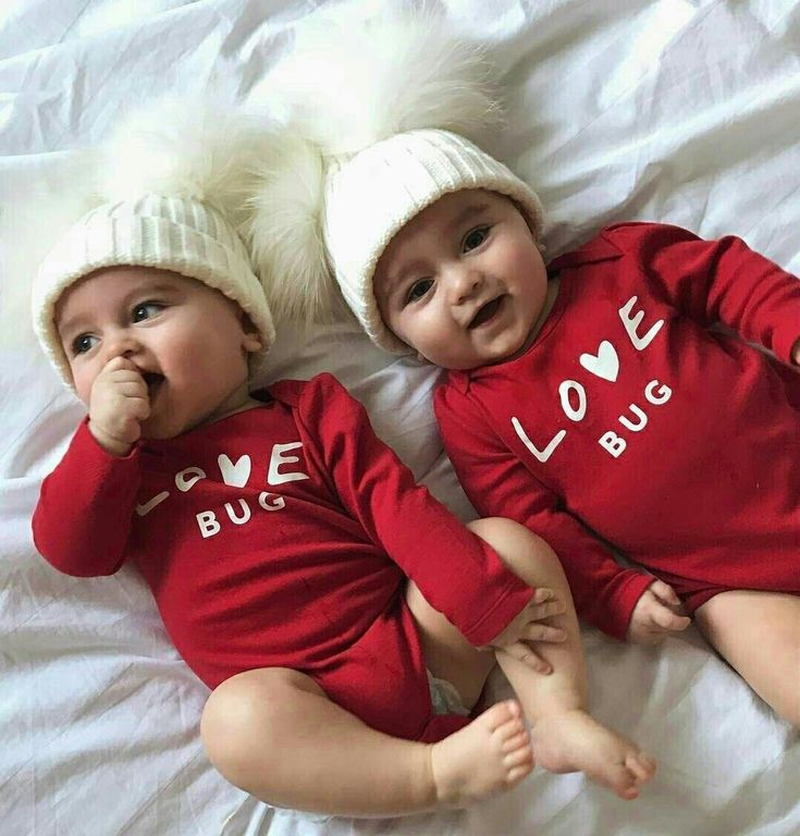 two babies laying on top of a bed wearing red shirts and white hats with the words love bug written on them