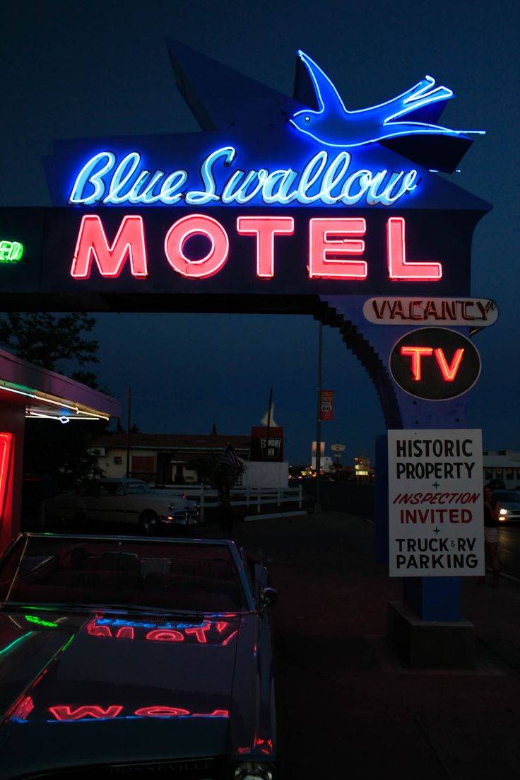 a motel sign lit up at night with neon lights on it and cars parked in front