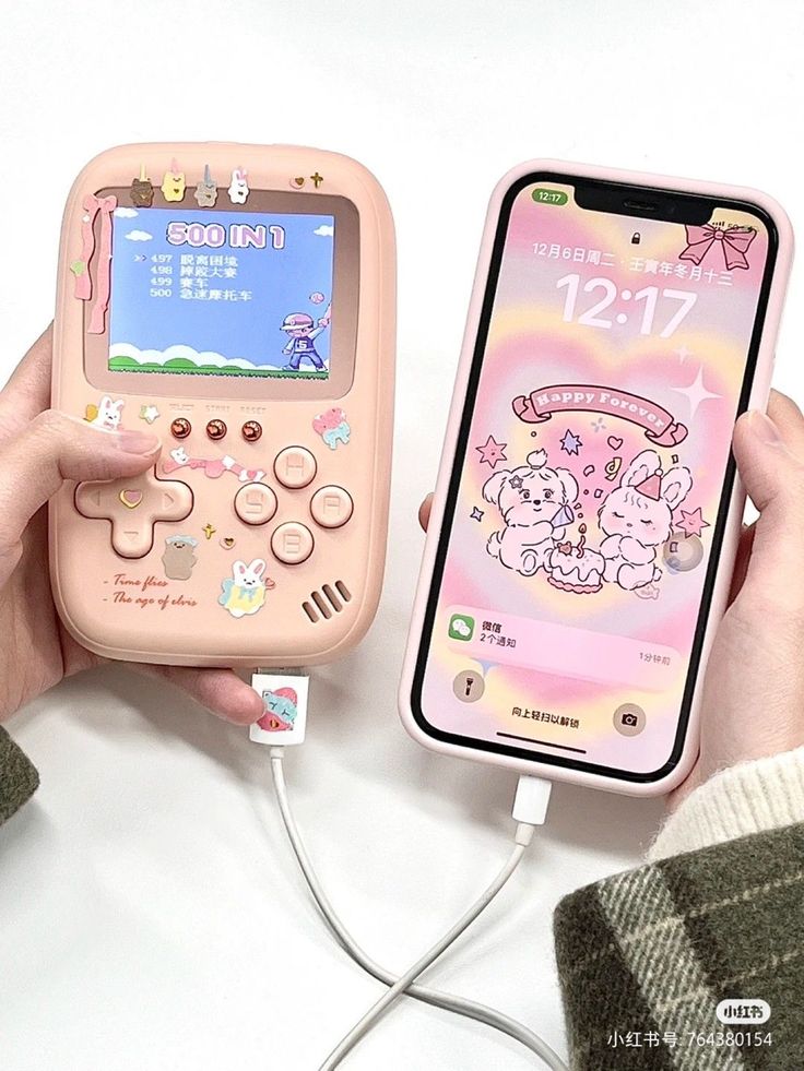 a person holding a pink phone next to an electronic device with a cartoon character on it