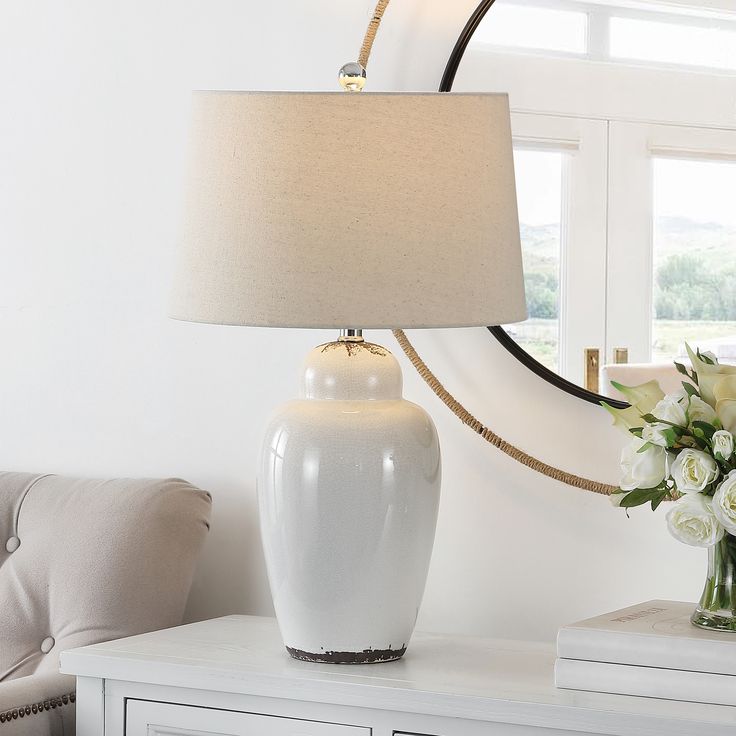 a white lamp sitting on top of a table next to a vase filled with flowers