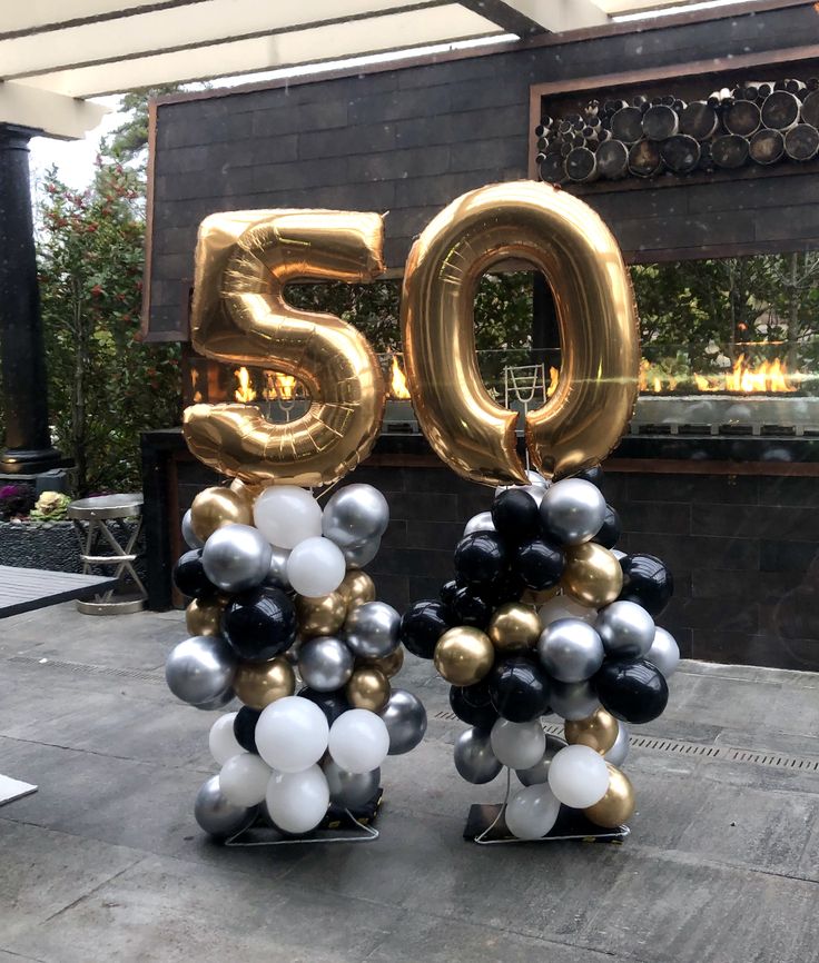 two black and white balloons with the number 50 in front of a building that is decorated with gold and silver balloons