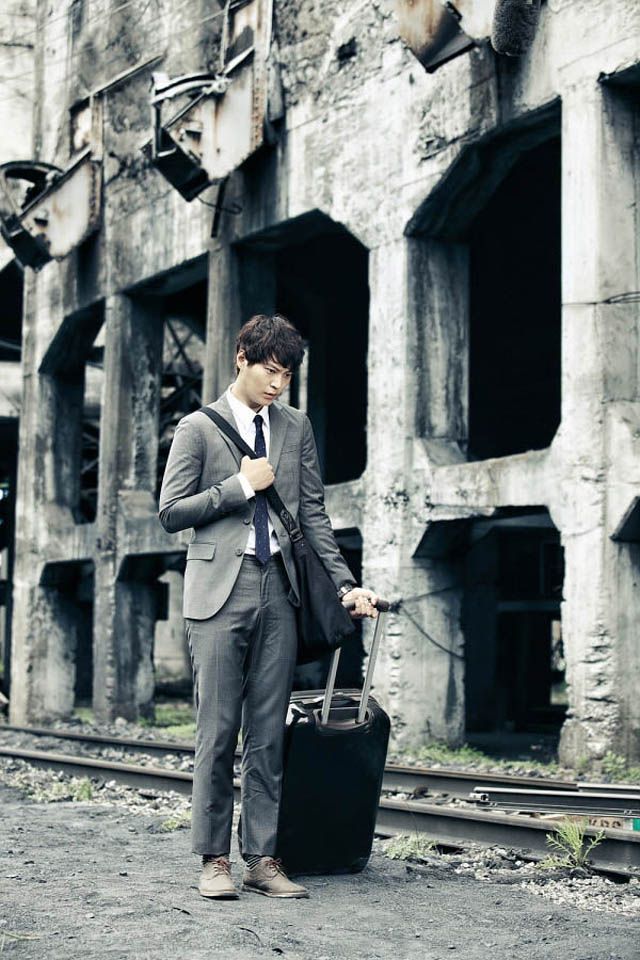 a man in a suit and tie standing next to an old building holding a suitcase