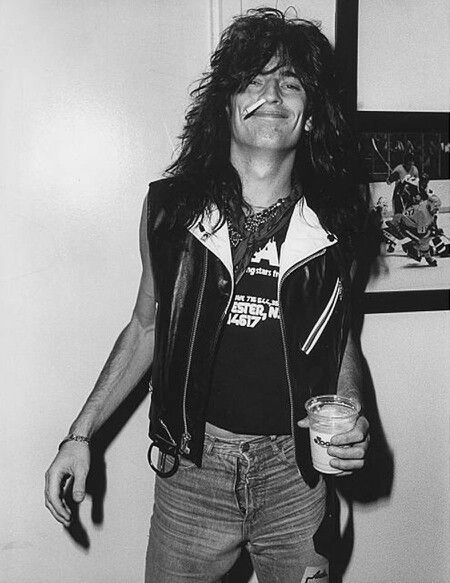 a black and white photo of a man with long hair holding a drink in his hand