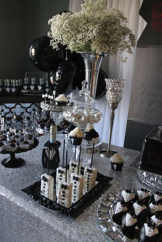 a table topped with cakes and desserts covered in black and white frosted icing