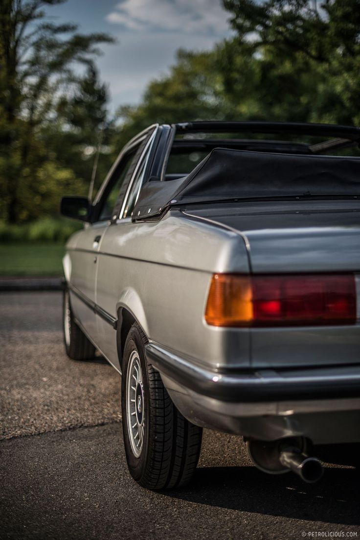 the back end of a silver car parked in a parking lot next to some trees