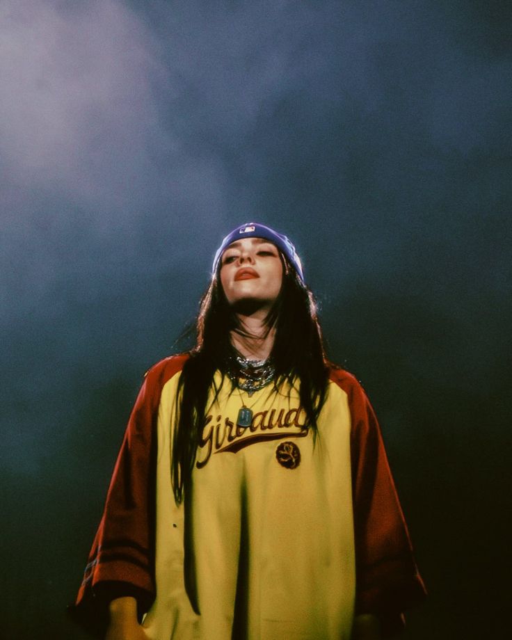 a man with long hair wearing a yellow shirt and blue hat looking up into the sky