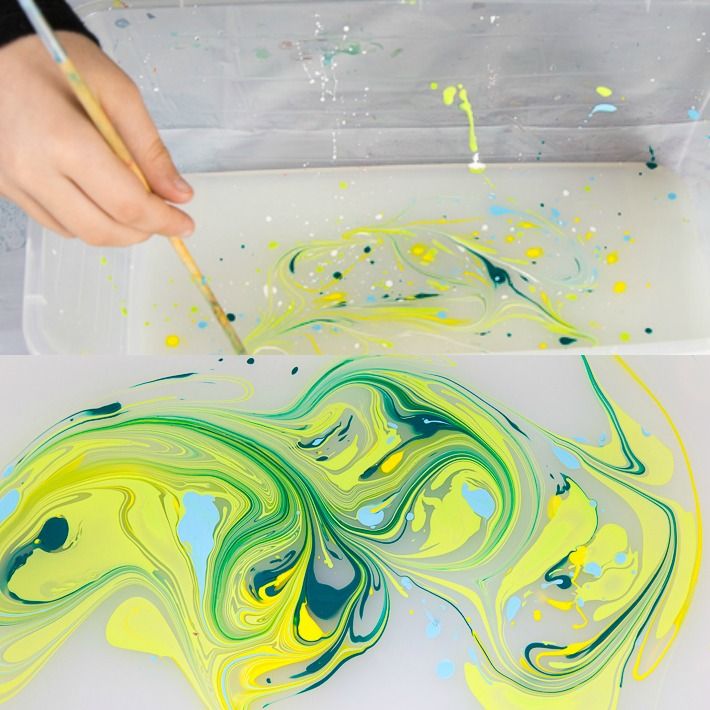 a child is painting with yellow and green paint on a white surface, while holding a brush