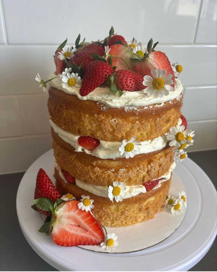 a three layer cake with strawberries and daisies on top, sitting on a plate