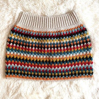 a multicolored crocheted skirt is laying on a white furnishing