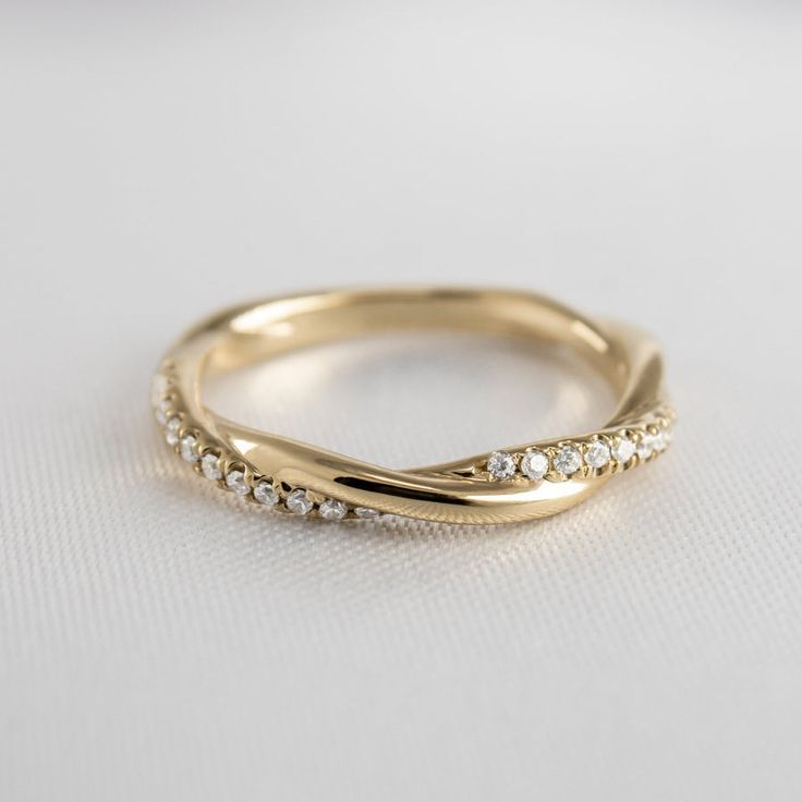 a yellow gold wedding band with diamonds on it's sides, sitting on a white surface